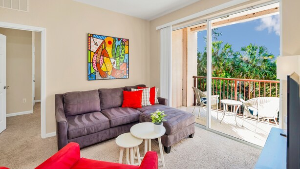 A modern living room with a grey sofa, red cushions, a small white table, and a colorful abstract painting on the wall. - 4024 Breakview Drive #208 (Orlando)