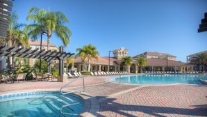 A pool area with lounge chairs and palm trees, surrounded by buildings with a Mediterranean architectural style. - 4024 Breakview Drive #208 (Orlando)