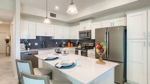 A modern kitchen with white cabinets, a central island, stainless steel appliances, and pendant lighting. - Modern Condo Near Disney Foosball Water Park! (Kissimmee)