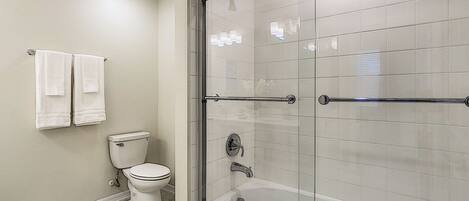 A modern bathroom with a glass-enclosed shower, a toilet, and a bathtub.