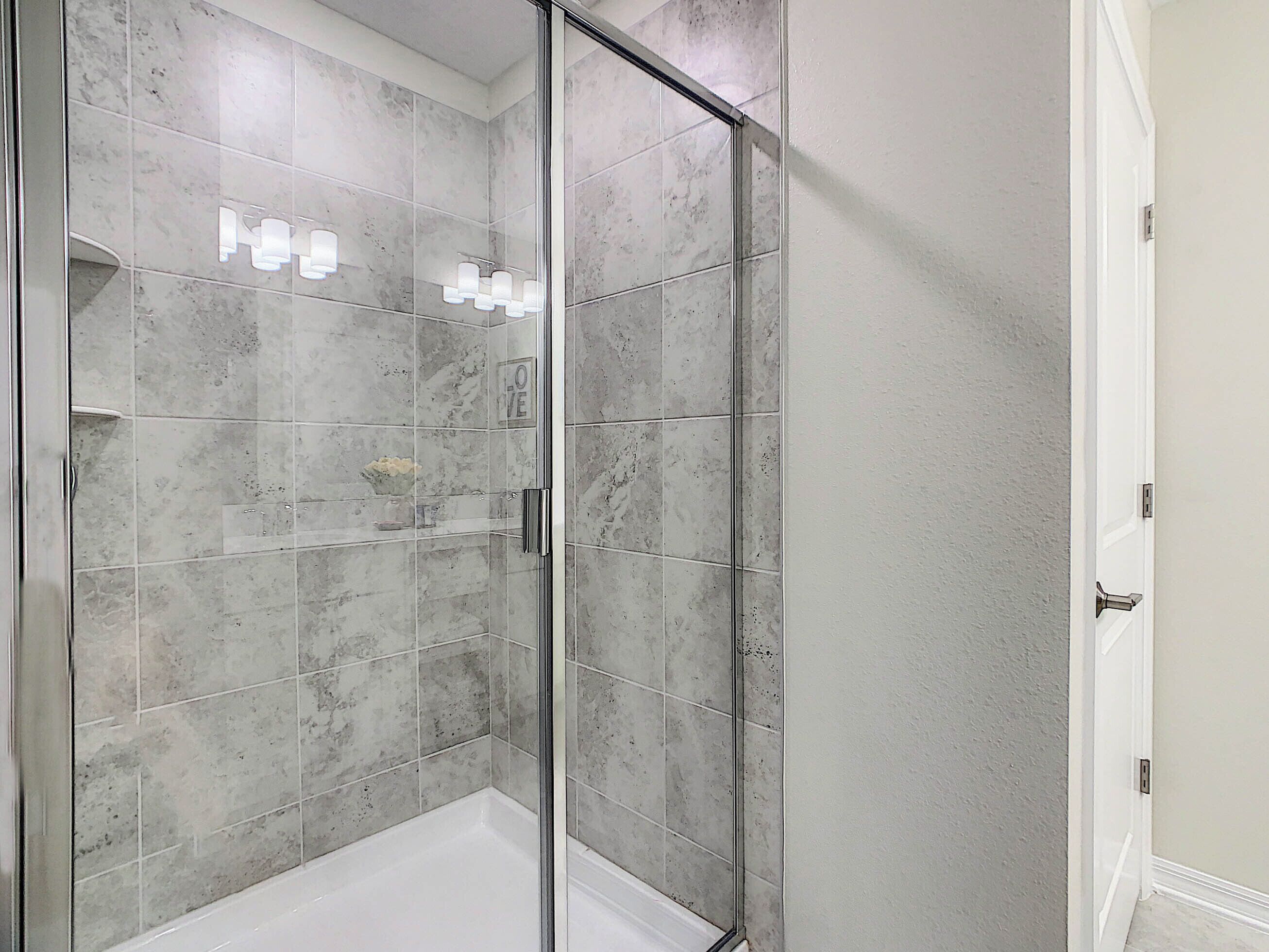 A walk-in shower with a glass door, tiled walls, and a white bathtub.