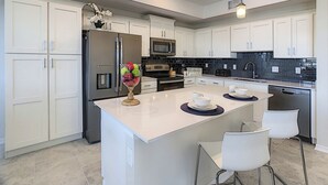 A modern kitchen with white cabinetry, stainless steel appliances, a central island with bar stools, and pendant lighting. - Water Slidelazy Riverfoosball5mi to Disney! (Kissimmee)