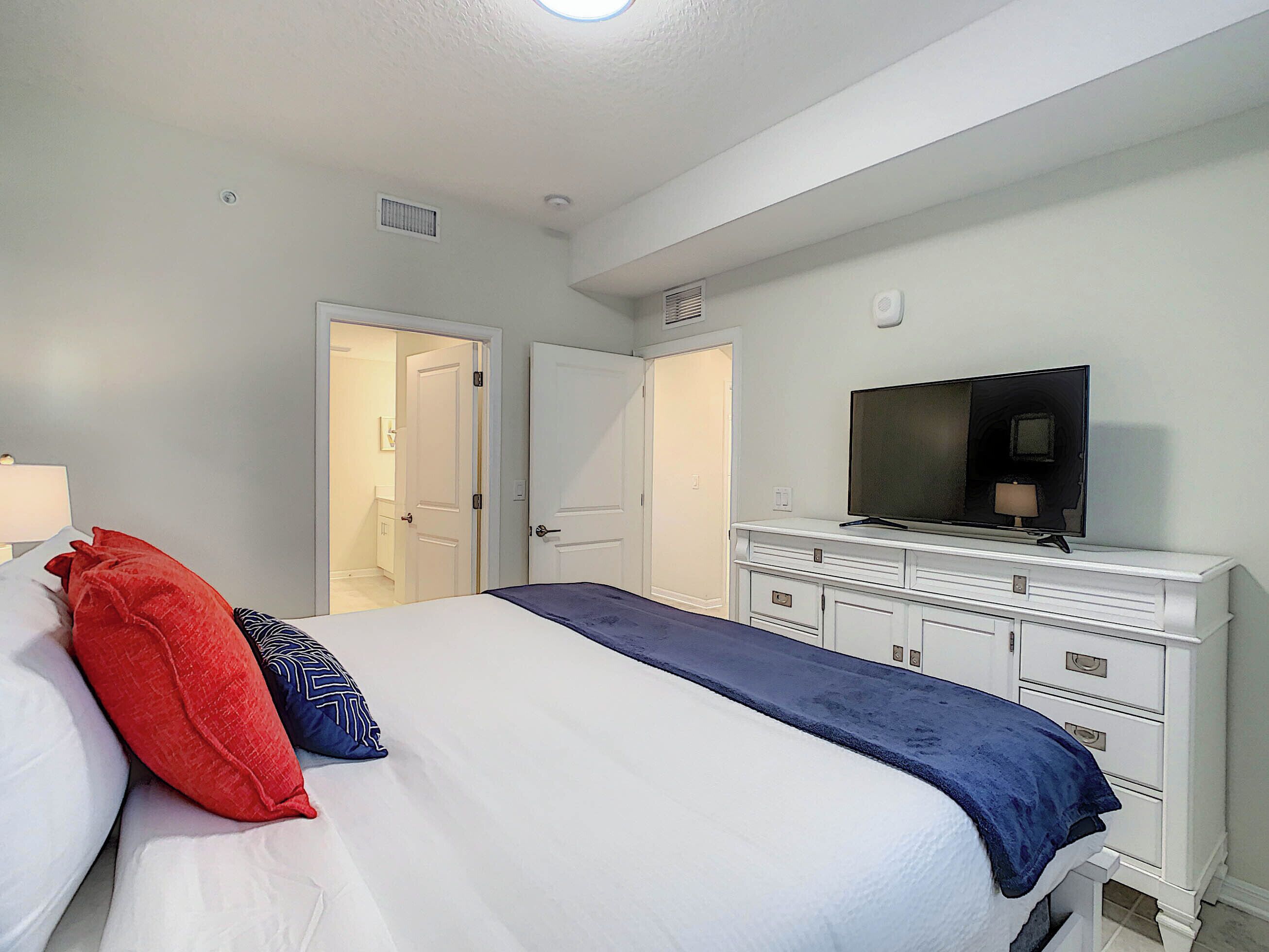 A hotel room with a bed, a TV on a dresser, and two doors leading to other rooms.