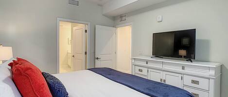 A hotel room with a bed, a TV on a dresser, and two doors leading to other rooms.