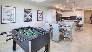 A modern kitchen with white cabinets, a central island, and a dining area with a foosball table. - Water Slidelazy Riverfoosball5mi to Disney! (Kissimmee)