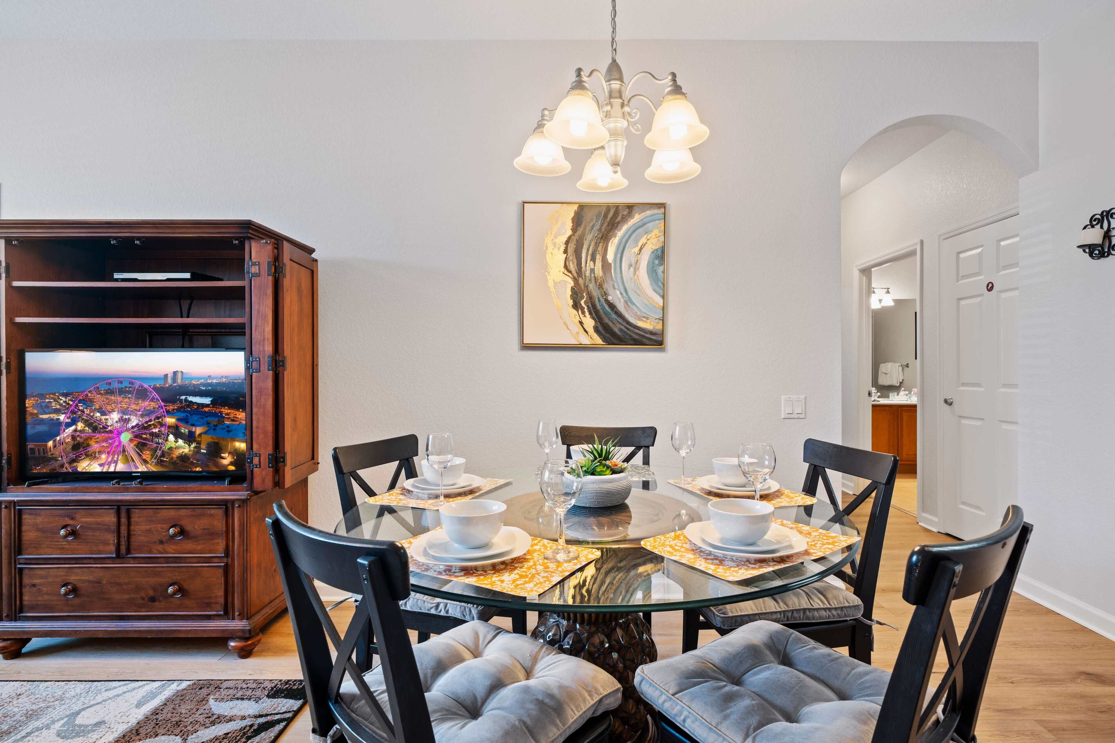 A dining area with a round glass table, black chairs, and a wooden cabinet with a TV.