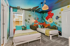 Un dormitorio con dos camas, un mural de una sirena y criaturas marinas, y un ventilador de techo.