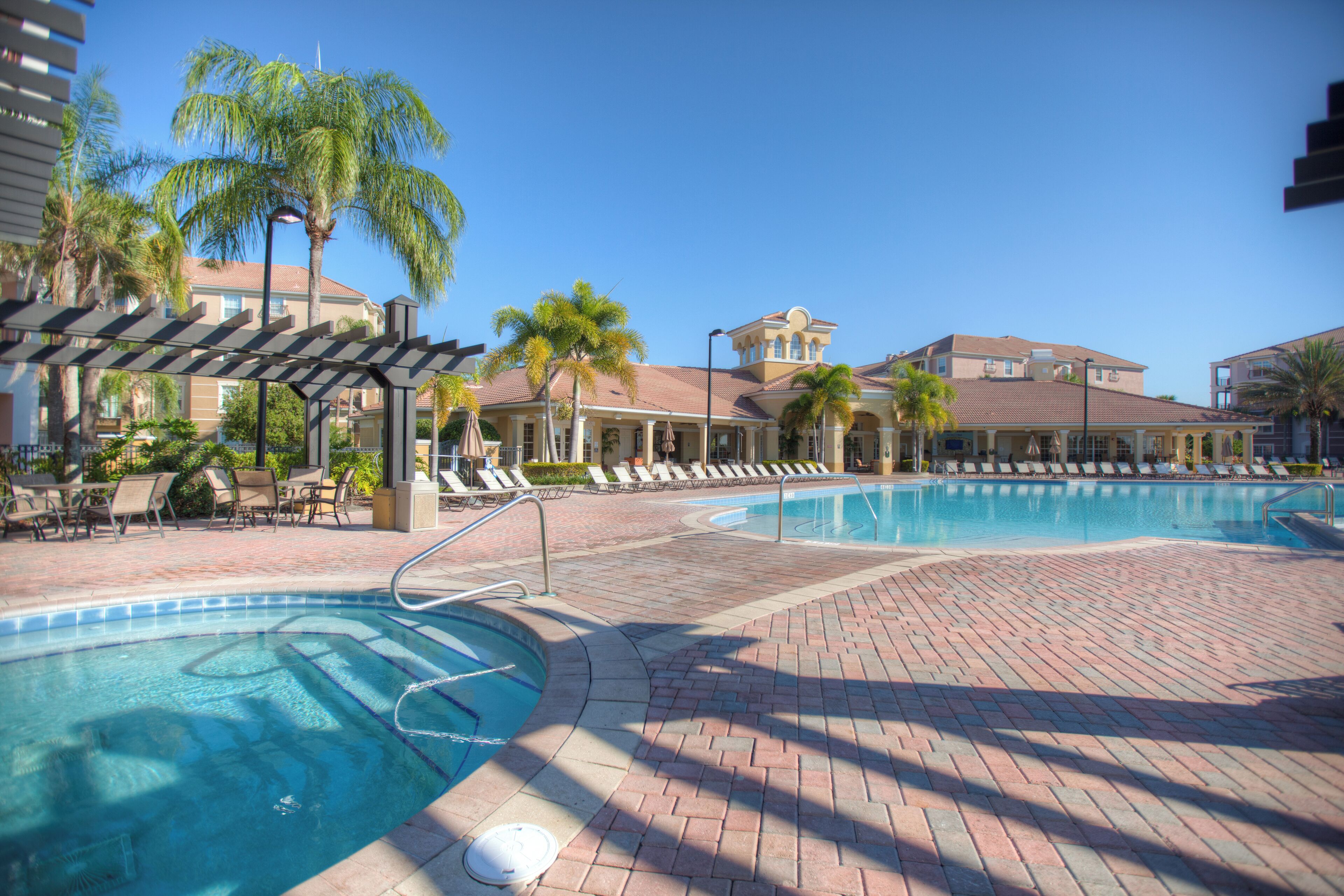 A pool area with lounge chairs and palm trees, surrounded by buildings with a Mediterranean architectural style.