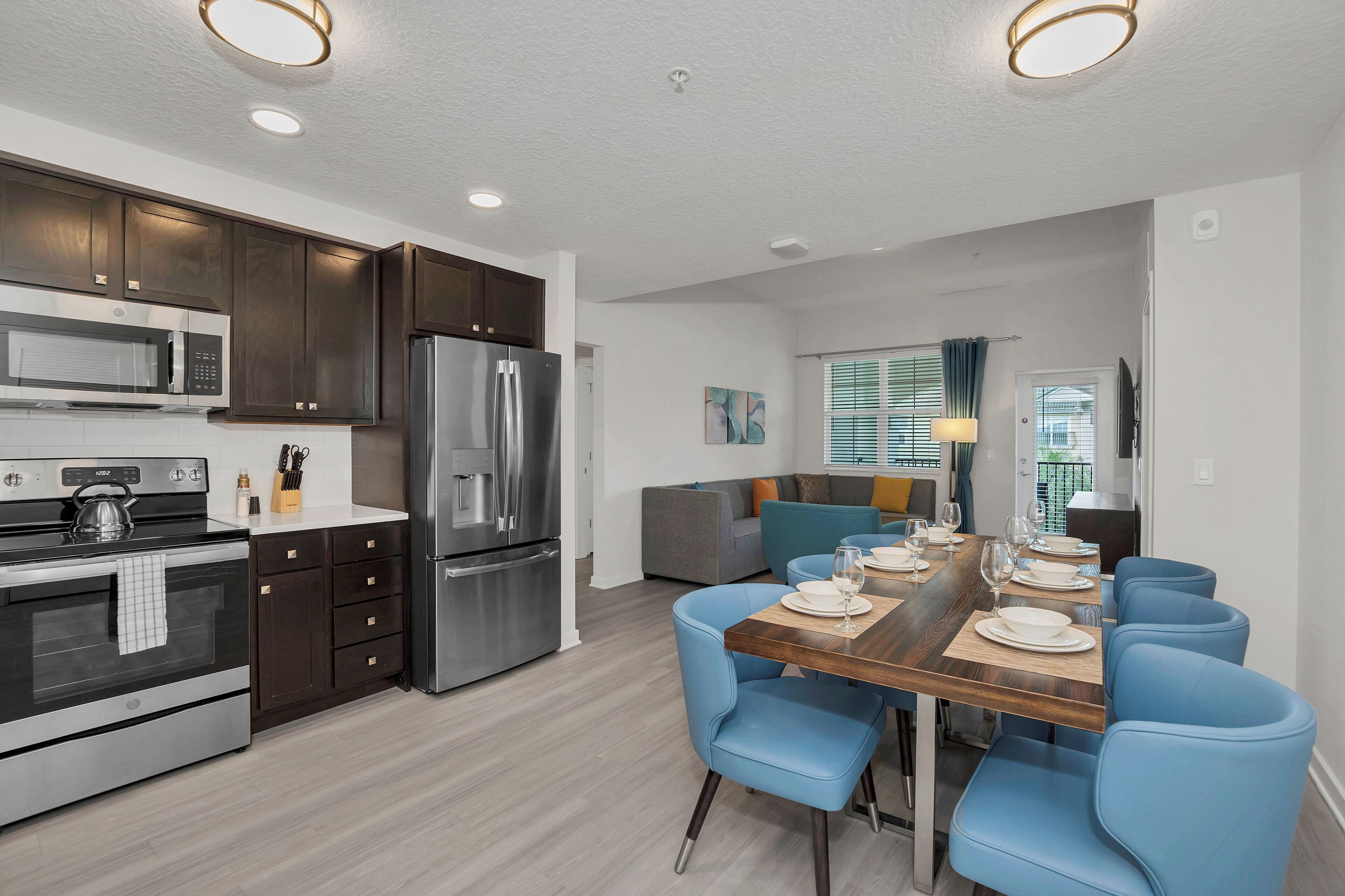 A modern kitchen with dark cabinets, stainless steel appliances, and a dining area with blue chairs and a wooden table.
