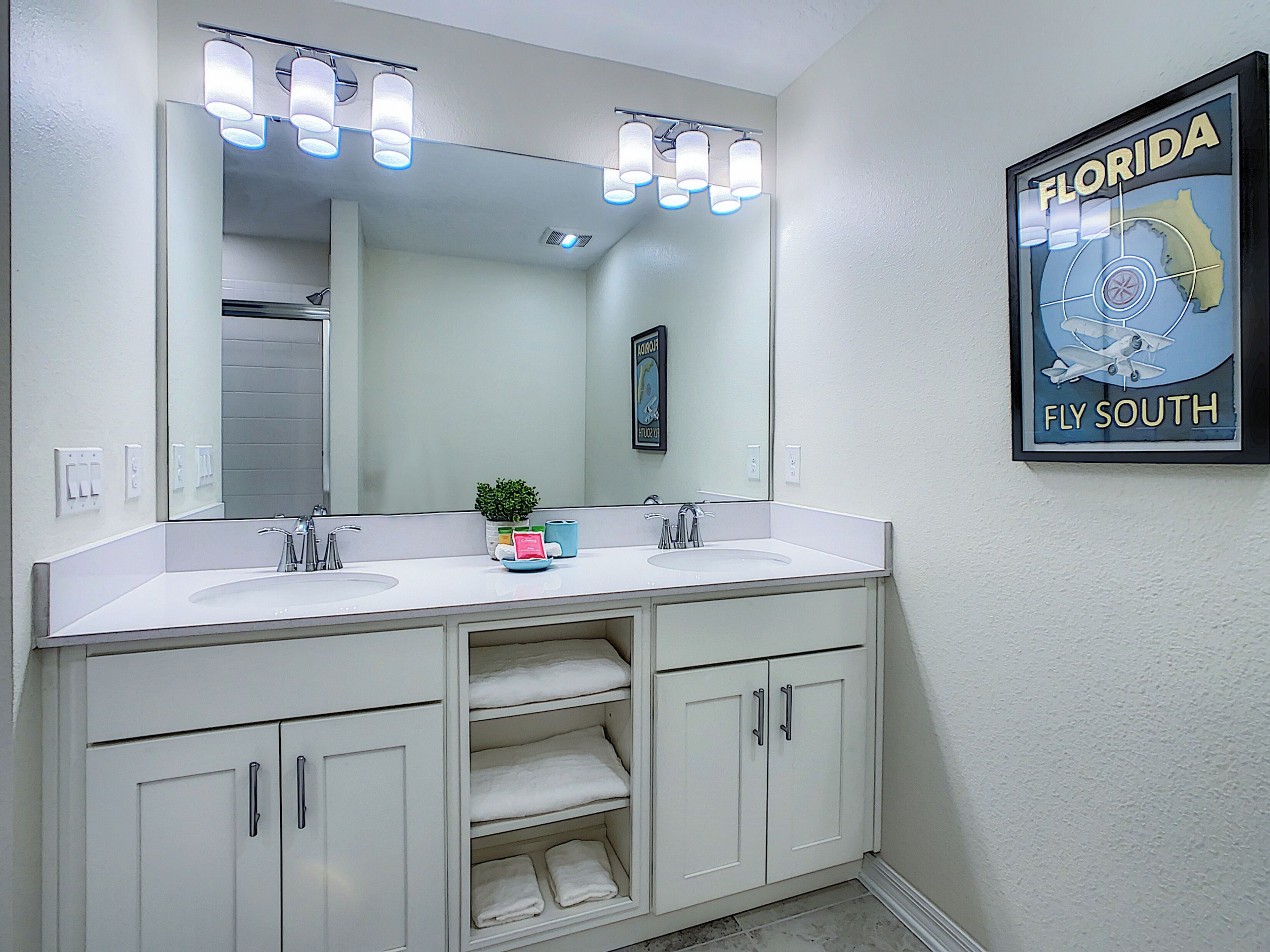 Un baño con tocador doble, un espejo grande y un cartel de Florida 'Fly South'.