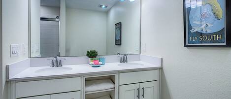 Un baño con tocador doble, un espejo grande y un cartel de Florida 'Fly South'.