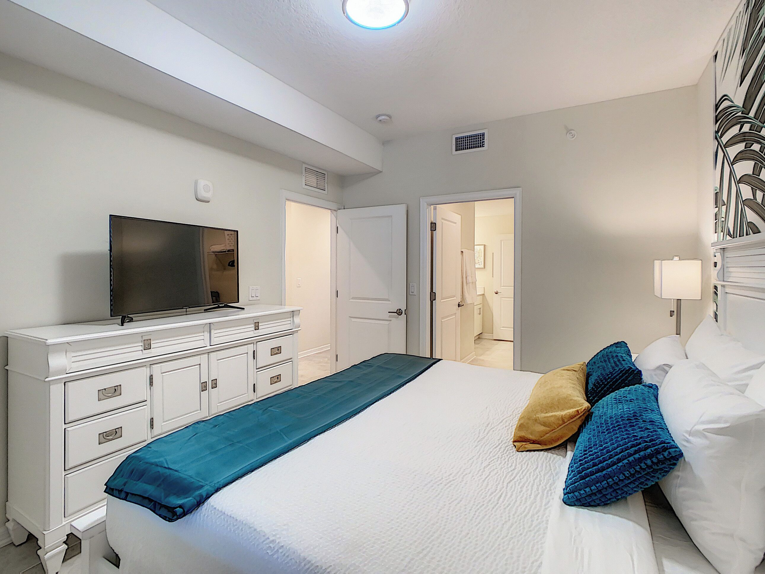 A hotel room with a bed, a TV on a dresser, and a door leading to a bathroom.