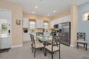A modern kitchen with white cabinets, a stainless steel refrigerator, and a dining table set for six. - 3078 Key Lime Loop (Kissimmee)