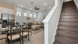 A modern kitchen with a refrigerator, dining table, and chairs. There is a staircase leading to an upper level. - 3078 Key Lime Loop (Kissimmee)