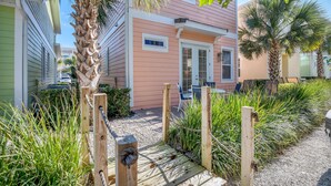 A pathway leading to a house with a wooden gate, surrounded by lush greenery and palm trees. - 3078 Key Lime Loop (Kissimmee)