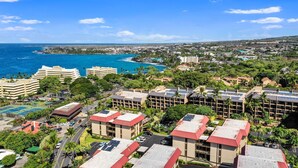 A coastal hotel with multiple buildings, a parking lot, and a view of the ocean. - Summer Deal Ocean View Kailua-Kona Condo Steps to Shops and Dining (Kailua-Kona)