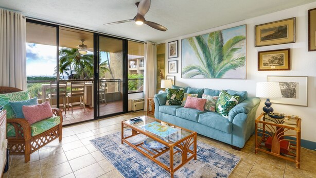 A living room with a blue sofa, a wooden coffee table, and a wicker chair. - Summer Deal Ocean View Kailua-Kona Condo Steps to Shops and Dining (Kailua-Kona)