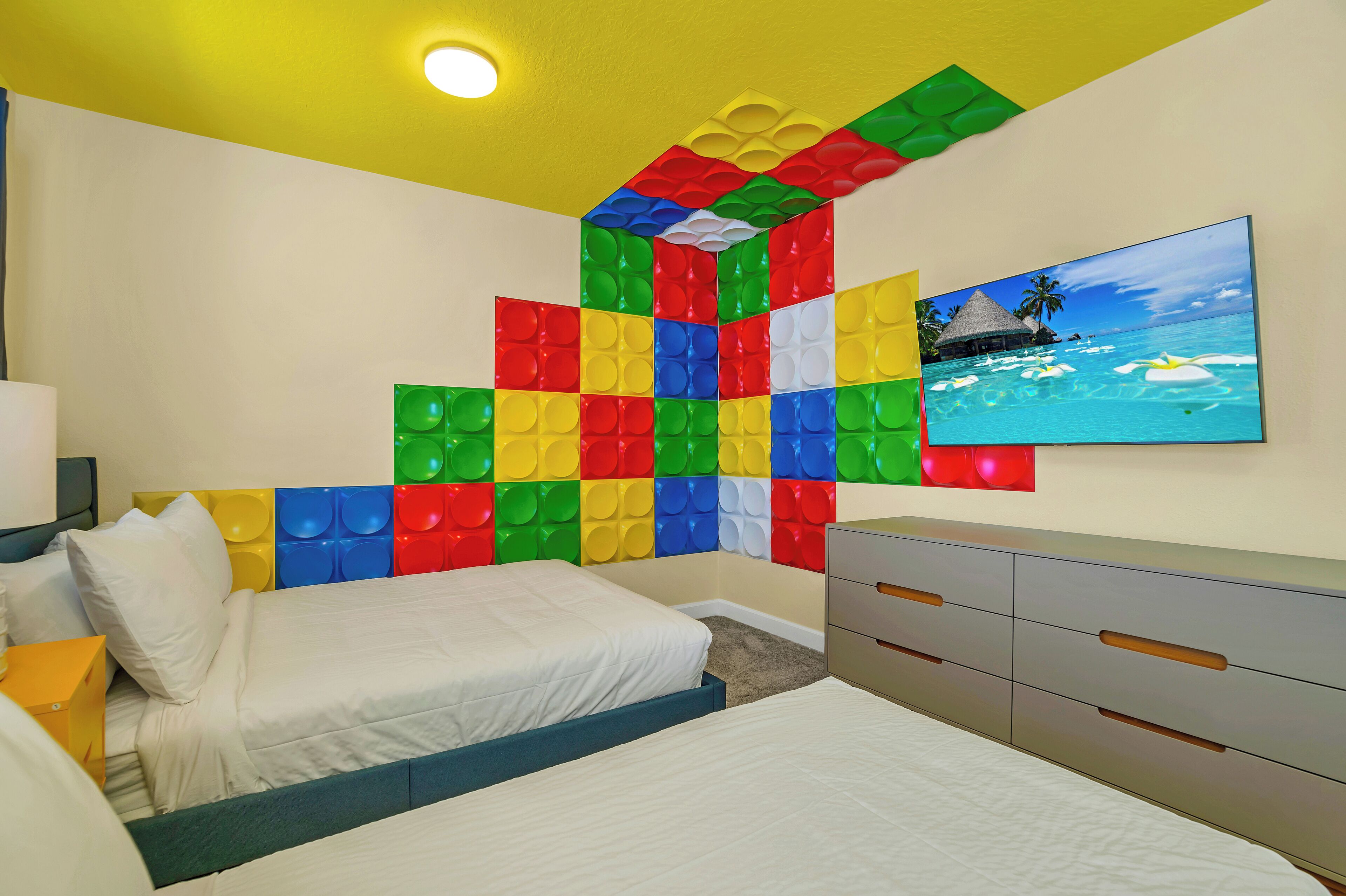 A bedroom with a bed, a dresser, a wall art of a beach scene, and a ceiling light.