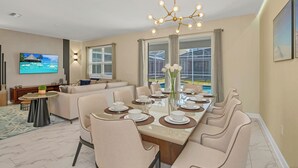 A modern dining area with a large table set for six, a sofa, and a TV mounted on the wall. - 700 Drop Shot Drive (Kissimmee)