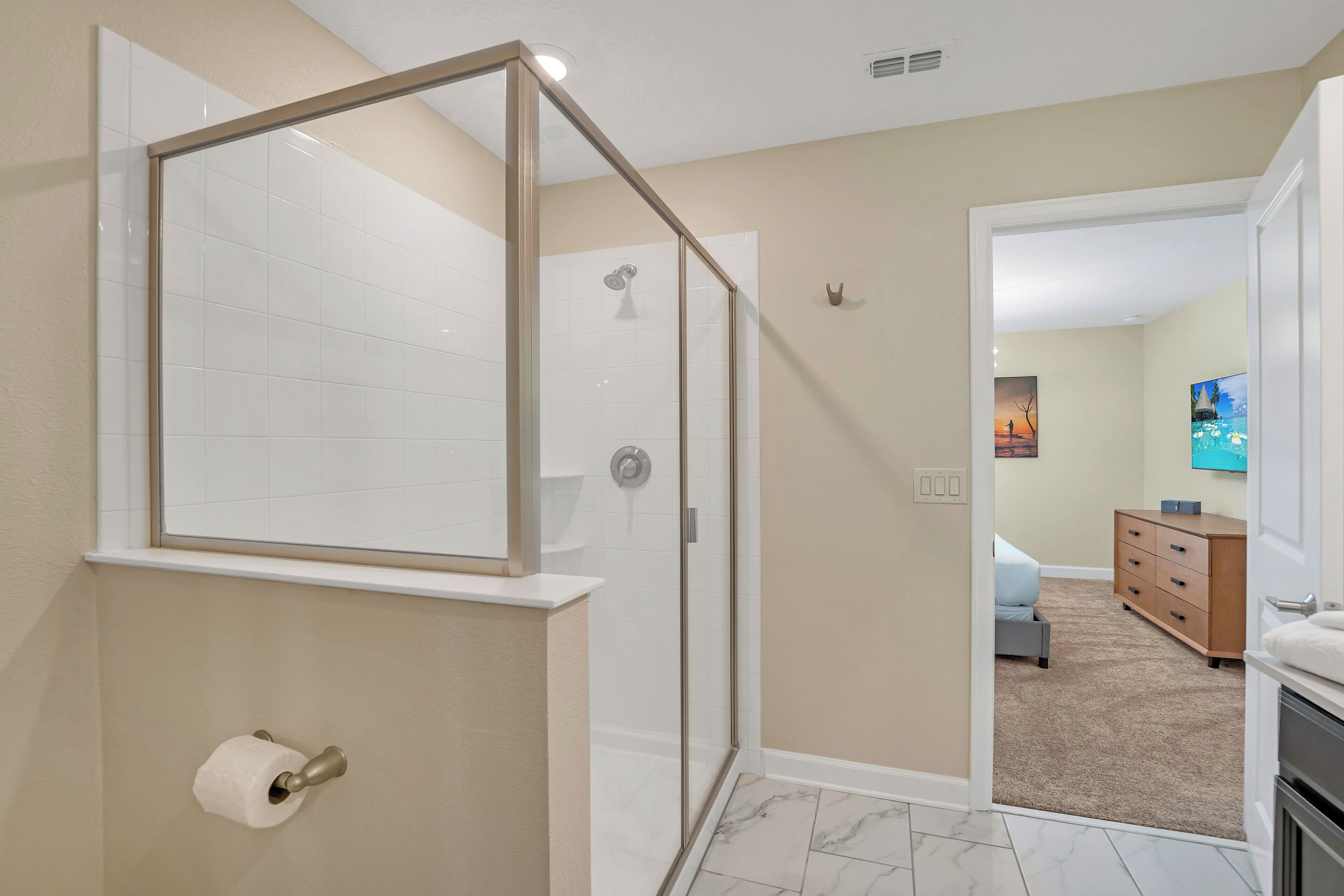 A modern bathroom with a glass shower enclosure, a toilet paper holder, and a marble-tiled floor.