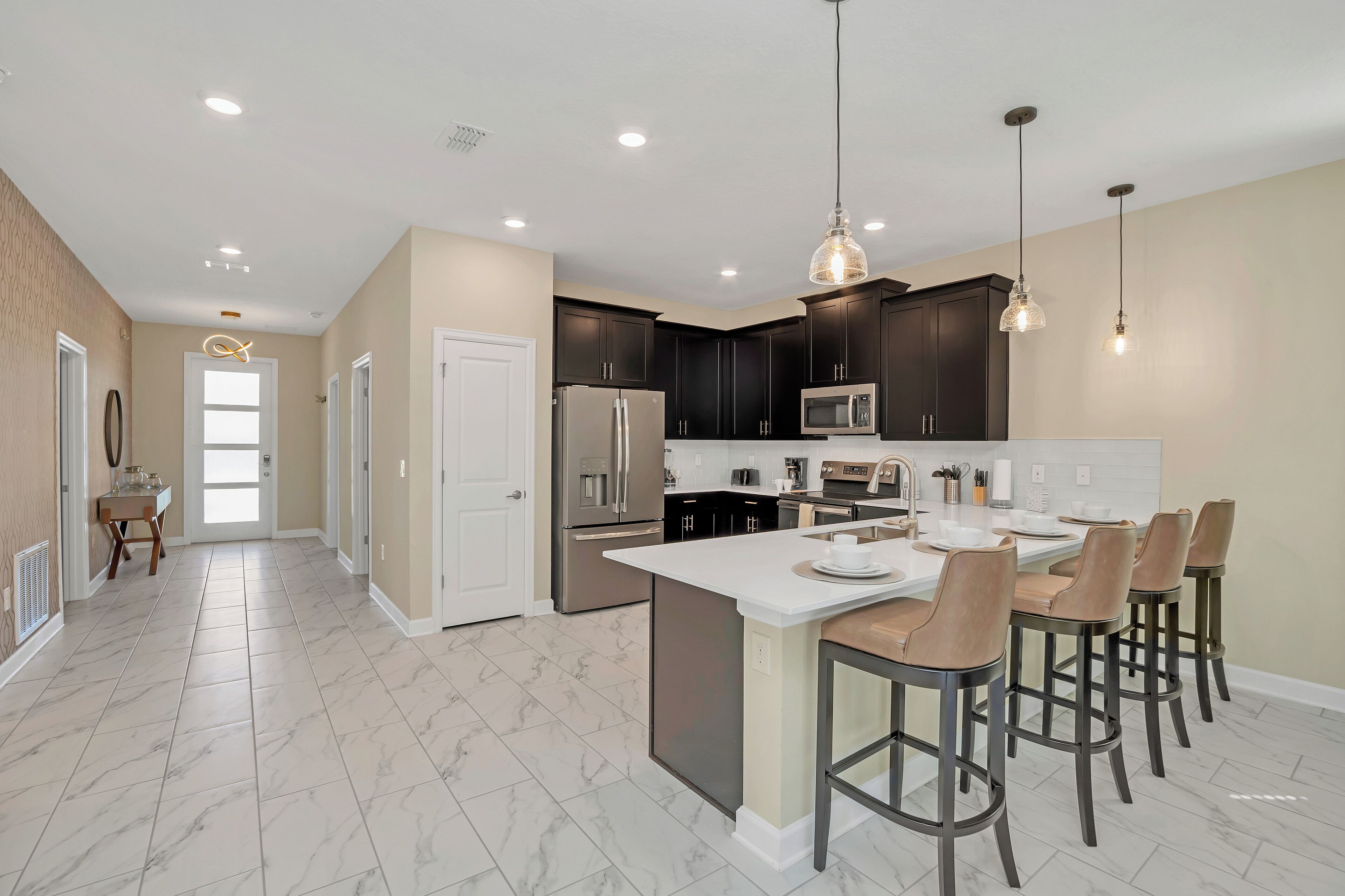 A modern kitchen with dark cabinets, a white island, and bar stools.