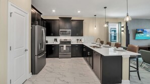 A modern kitchen with dark cabinets, stainless steel appliances, and a large island. - 700 Drop Shot Drive (Kissimmee)