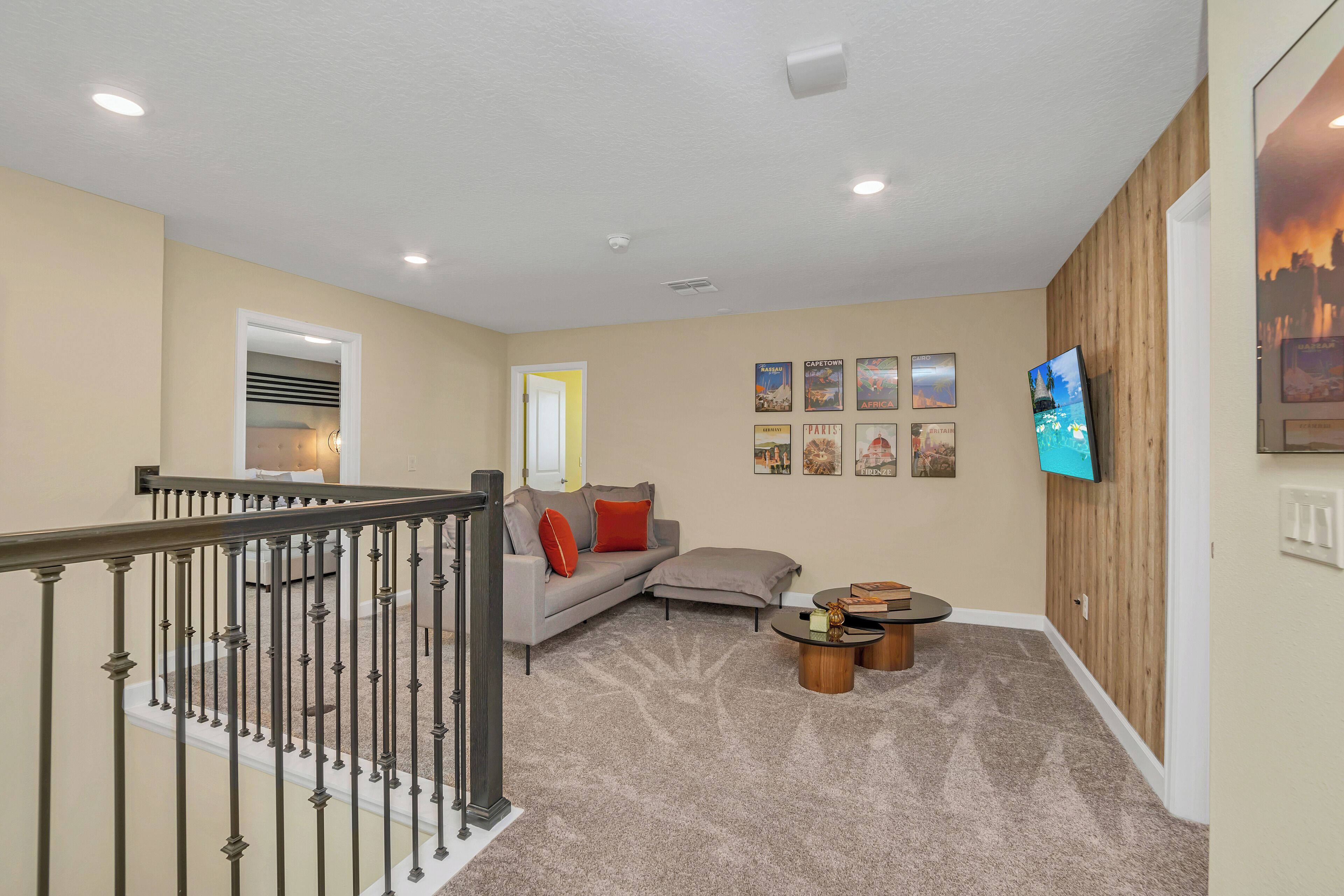 A well-lit hallway with a staircase, a grey sectional sofa, a small coffee table, and a flat-screen TV mounted on the wall.