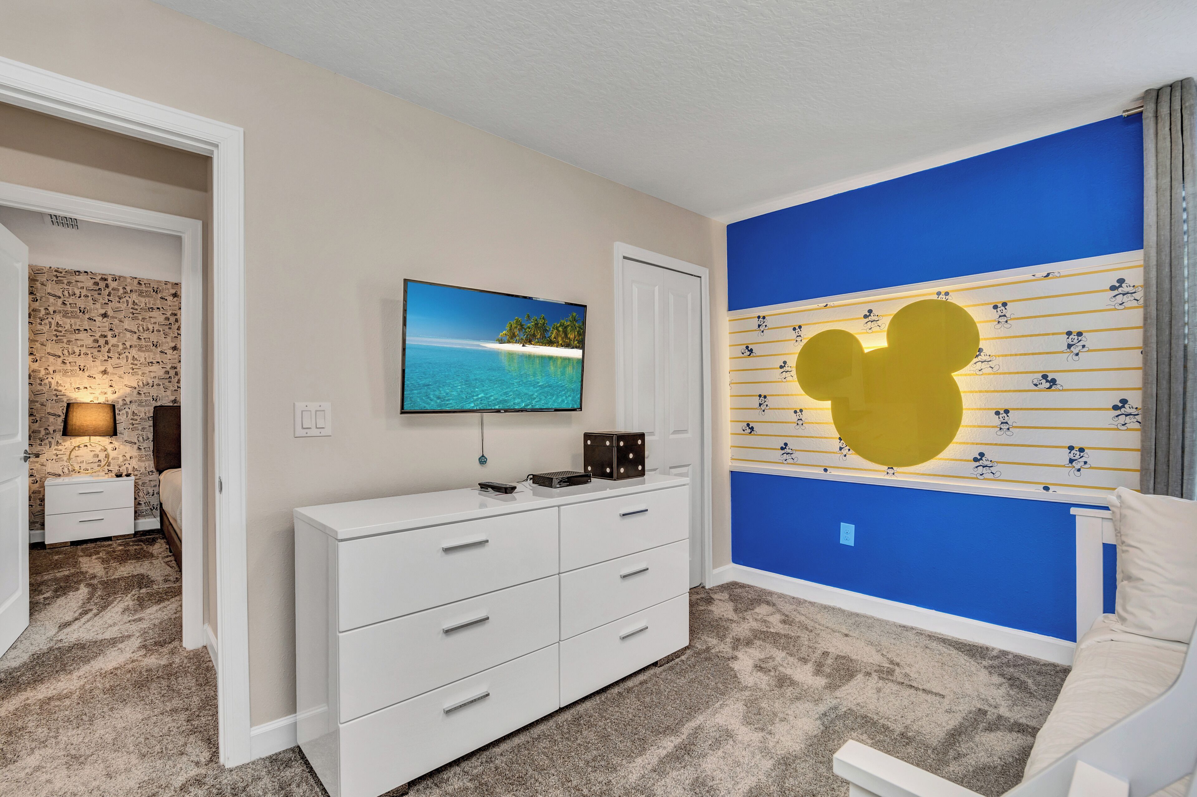 Ein Schlafzimmer mit einem großen Flachbildfernseher, einer weißen Kommode, einer Mickey Mouse Wandsticker und einem Fenster mit Meerblick.