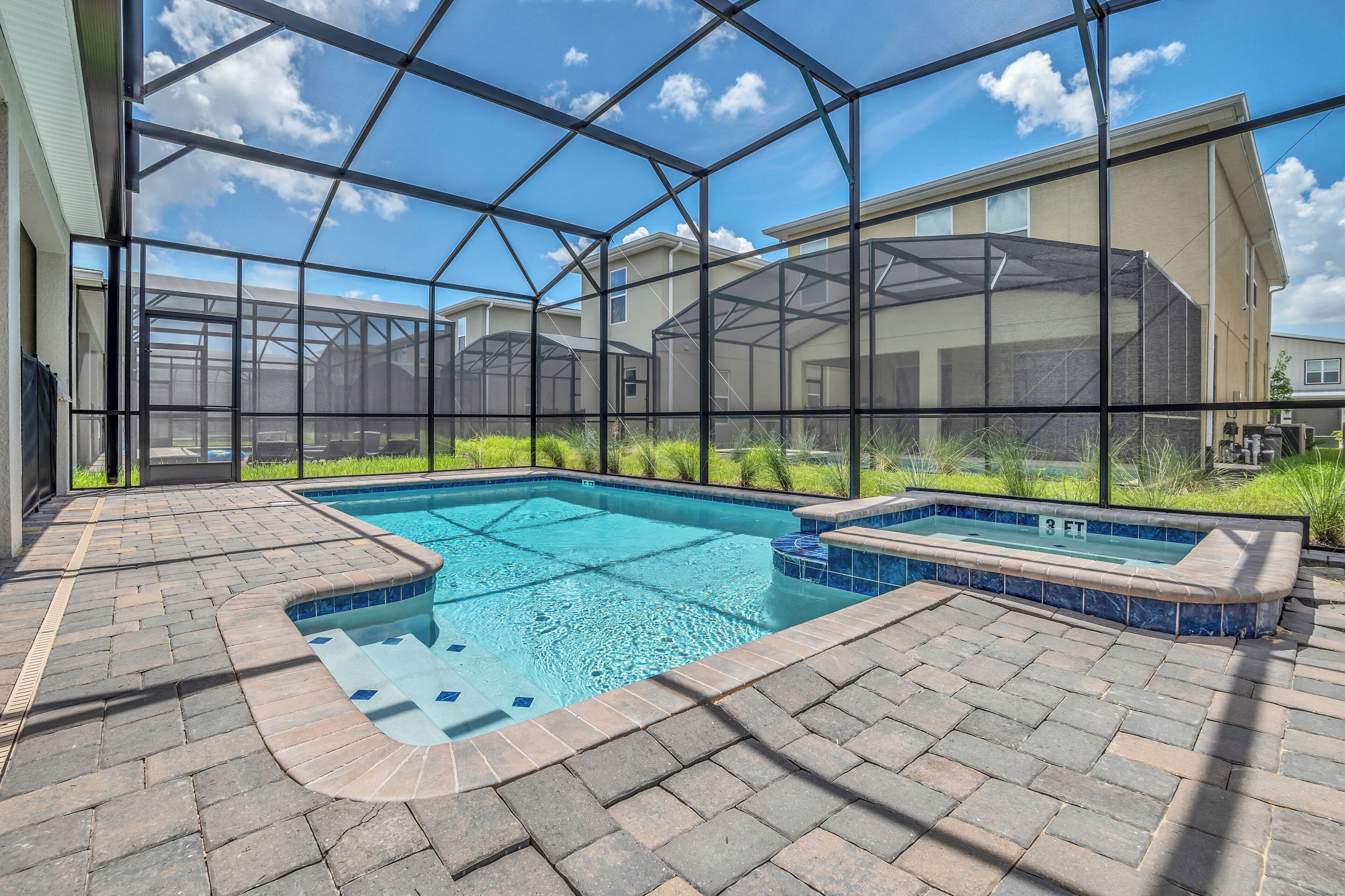 An indoor swimming pool with a glass enclosure, a hot tub, and a brick patio area.