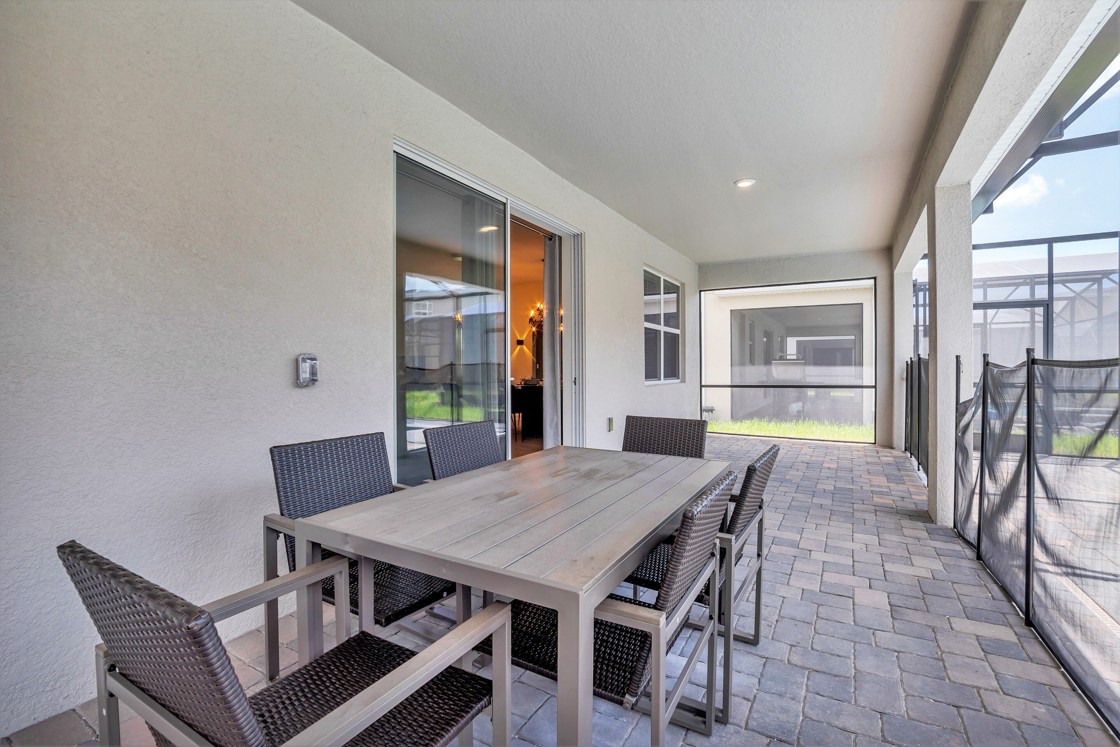 A patio with a wooden table and chairs, a glass door leading to an interior space, and a view of the outdoors.