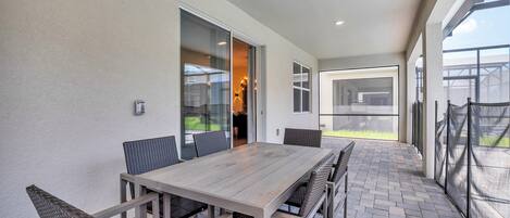 A patio with a wooden table and chairs, a glass door leading to an interior space, and a view of the outdoors.
