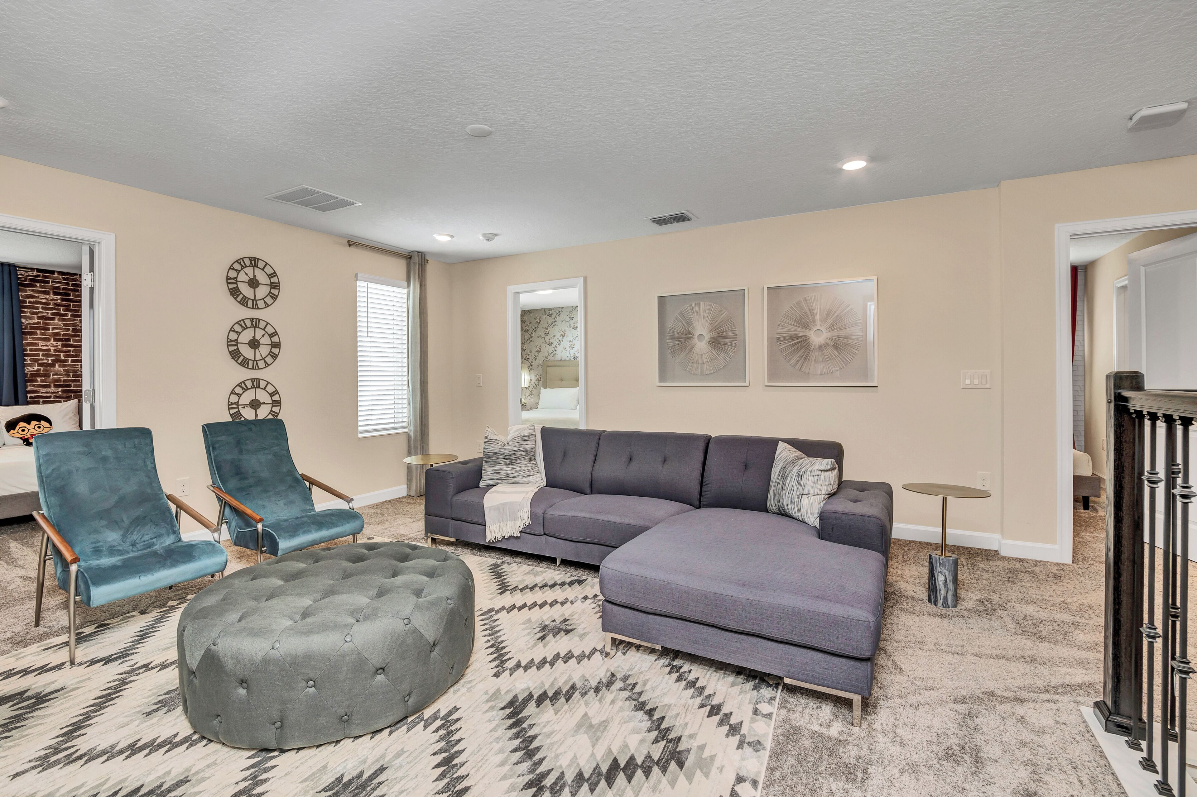 A living room with a sectional sofa, two armchairs, a round ottoman, and a patterned rug.