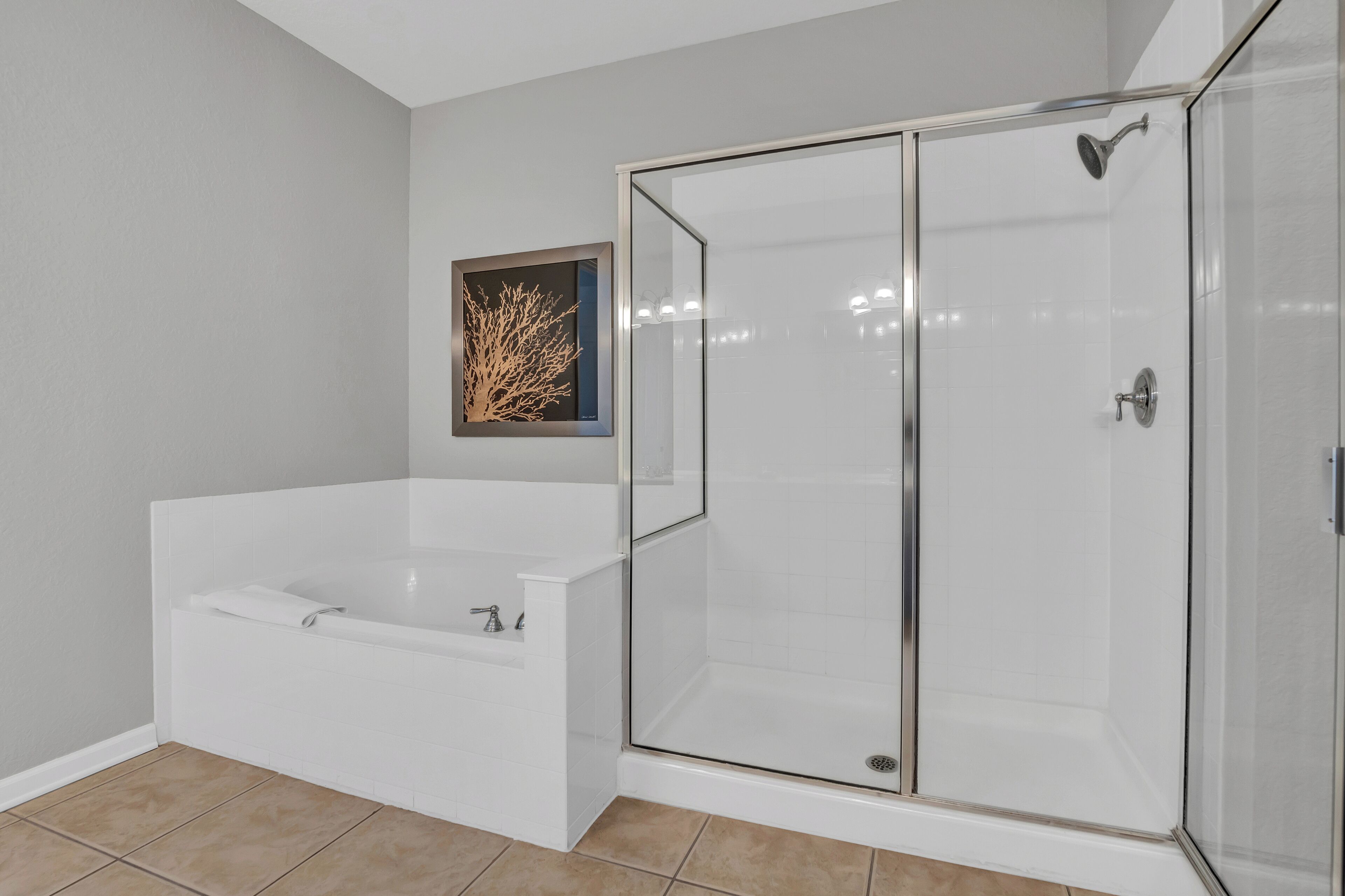 A modern bathroom with a glass-enclosed shower, a white bathtub, and a framed artwork on the wall.