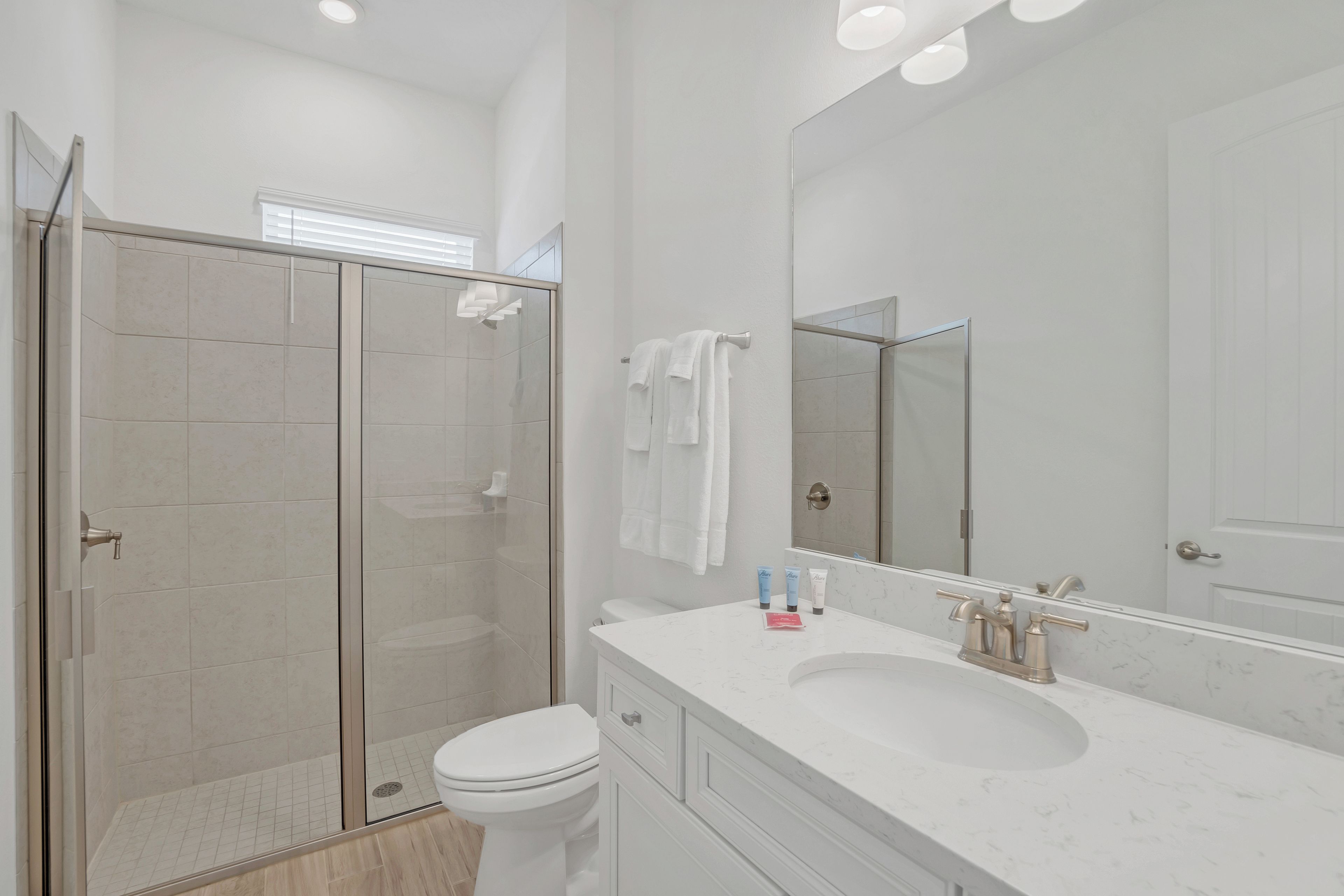A modern bathroom with a glass-enclosed shower, a white toilet, a marble sink, and a large mirror.