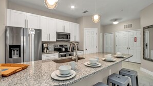 A modern kitchen with stainless steel appliances, granite countertops, and bar stools. - Luxurious Condo Near Disneyfree Waterpark Access (Kissimmee)