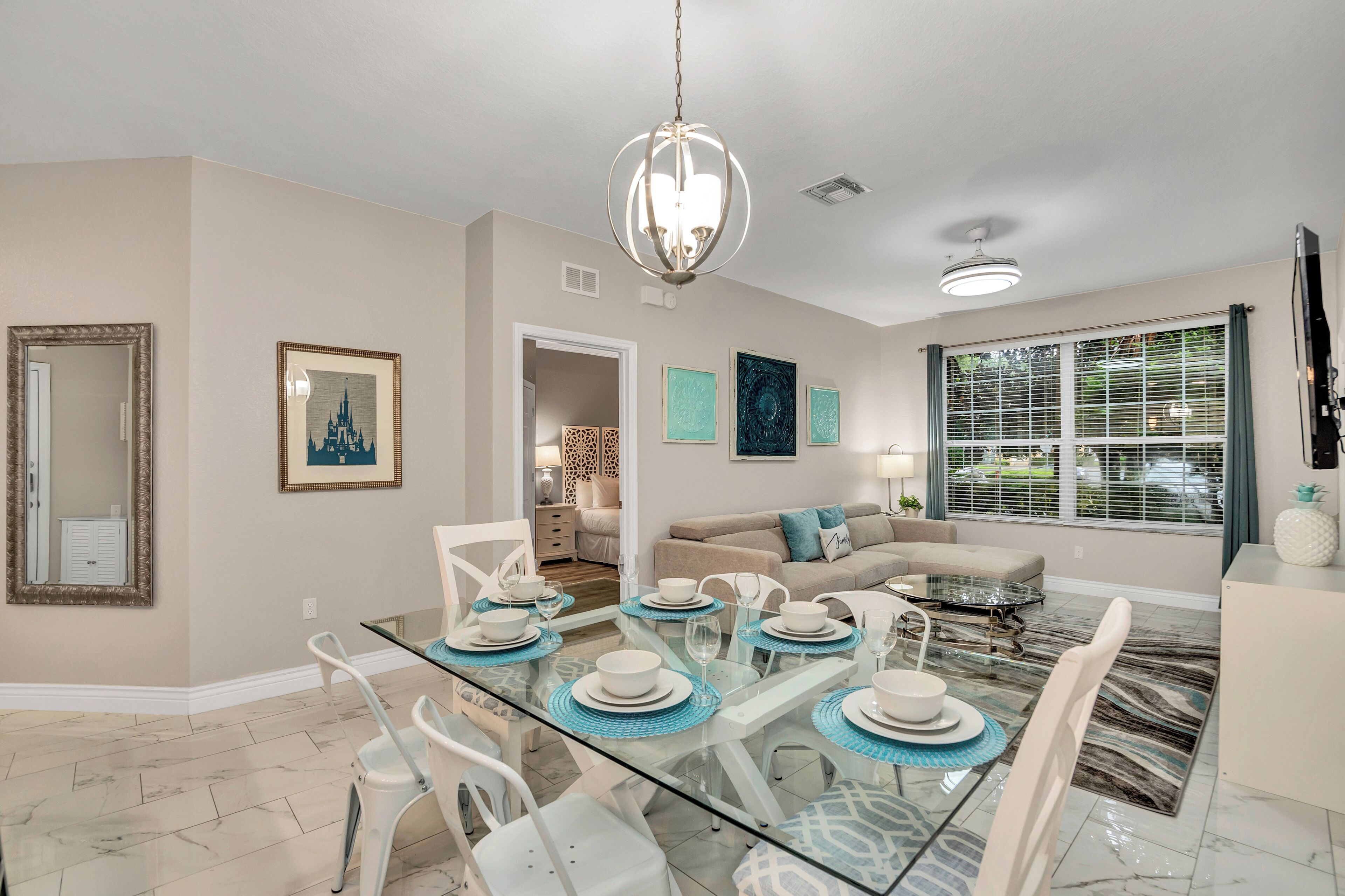 A dining area with a glass table set for six, a sofa, and a TV in the background.