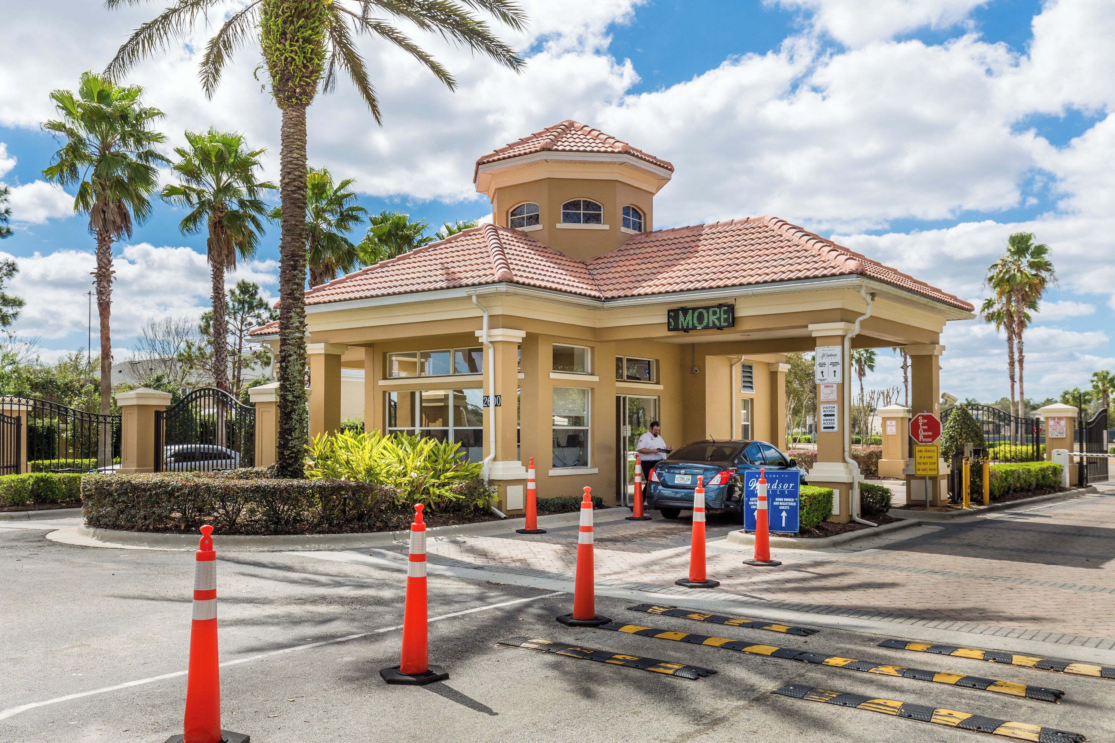 A hotel entrance with a red-tiled roof, palm trees, and orange traffic cones.