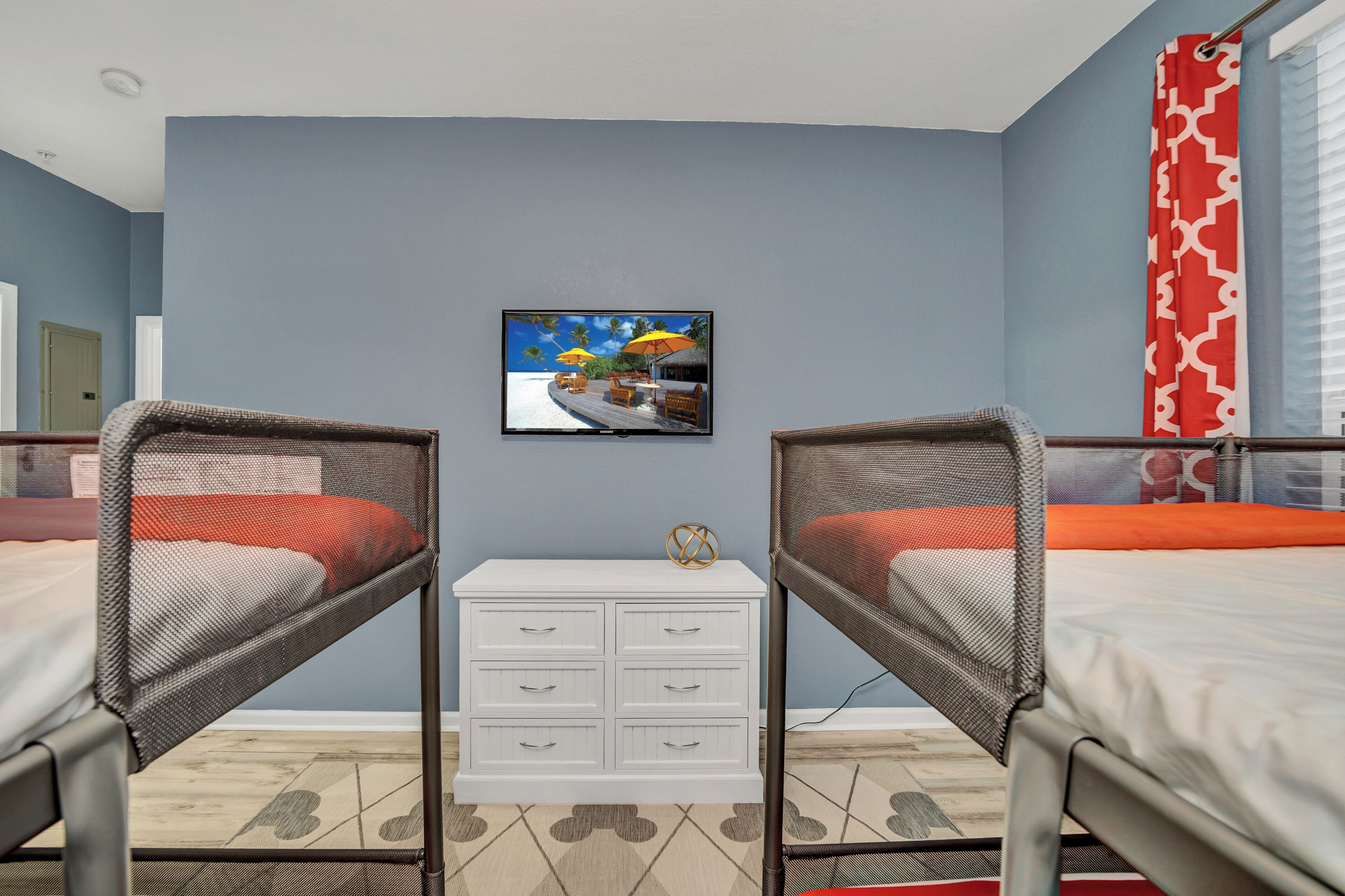 Une chambre avec deux lits superposés, un téléviseur fixé au mur et une petite commode blanche.