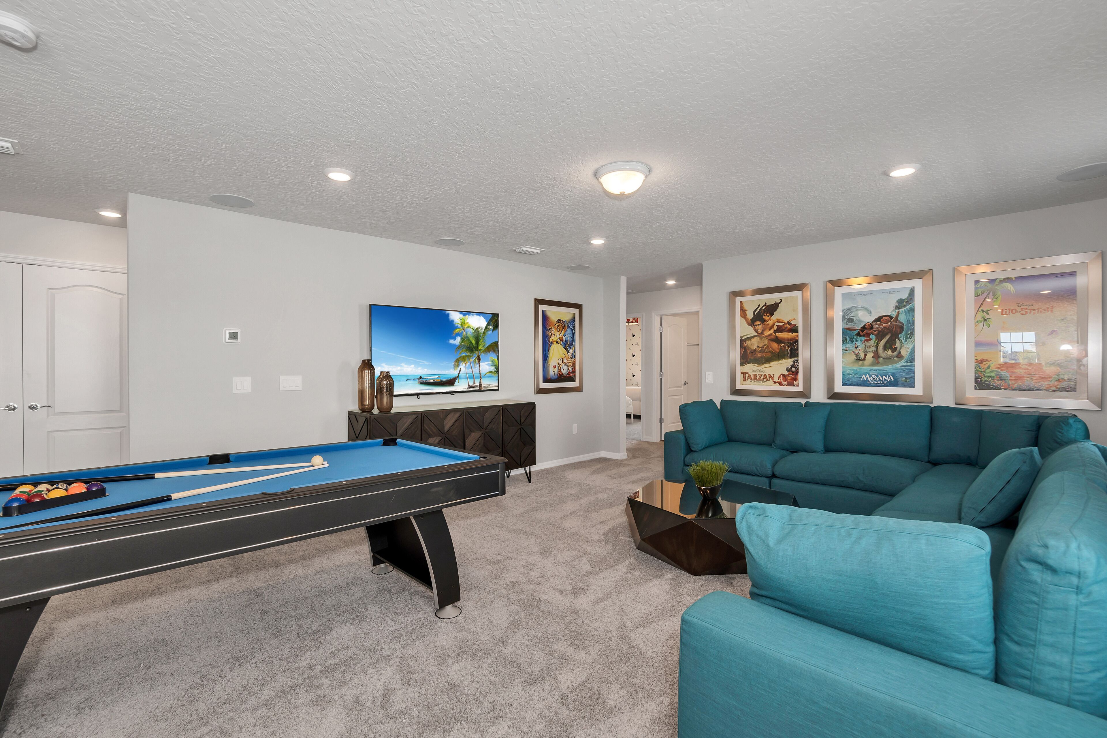 A pool table with a blue felt surface, a teal sofa, and framed artwork on the walls.