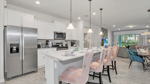 Une cuisine moderne avec des meubles blancs, des appareils en acier inoxydable et un îlot central doté de chaises recouvertes d’un tissu rose.