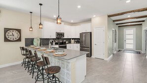 A modern kitchen with white cabinets, stainless steel appliances, and a central island with bar stools. - Large Villa, Private Pool+game Room+movie Theater! (Kissimmee)