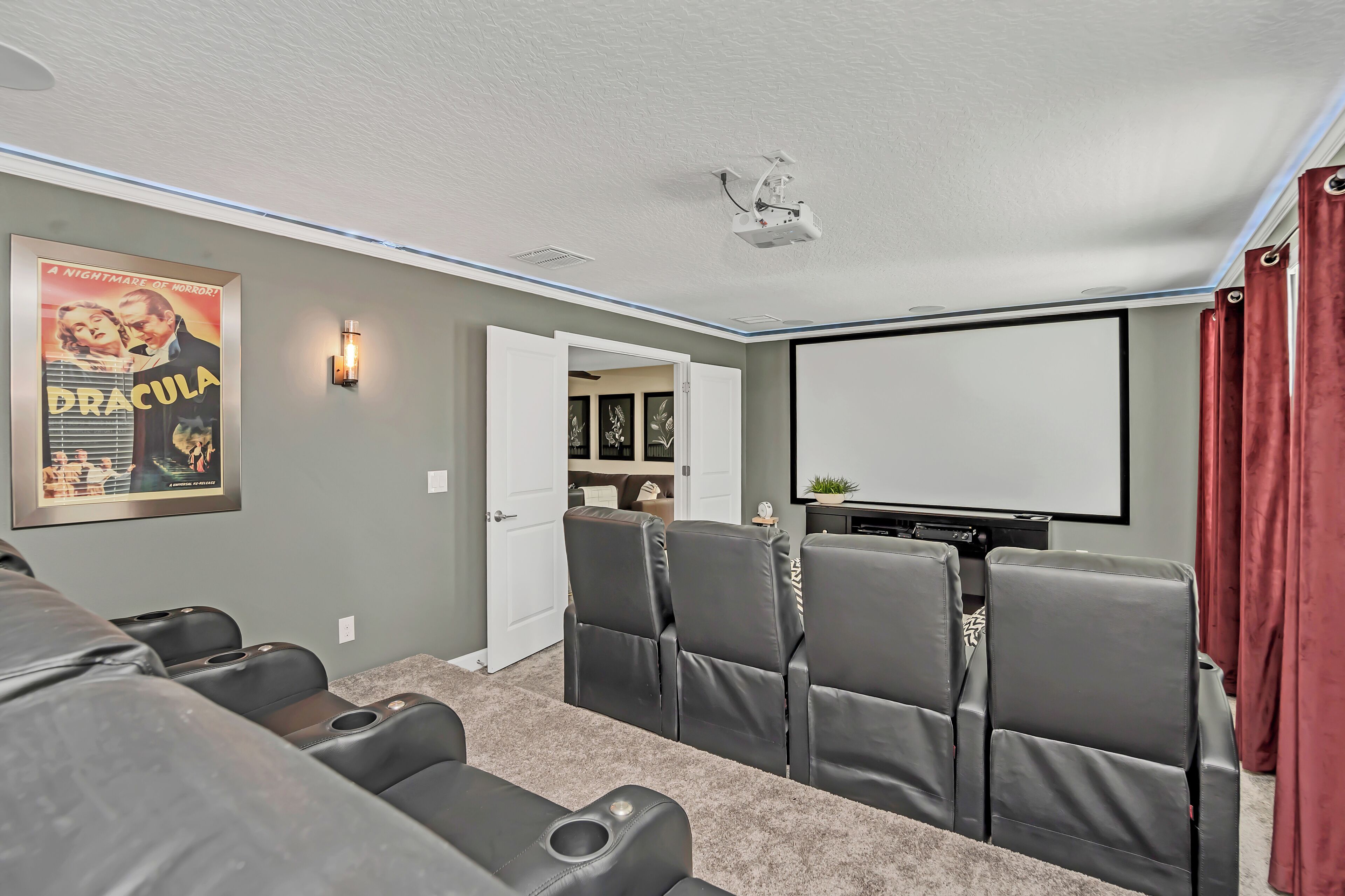 A home theater room with a large screen, reclining chairs, a popcorn machine, and a poster of 'Dracula'.