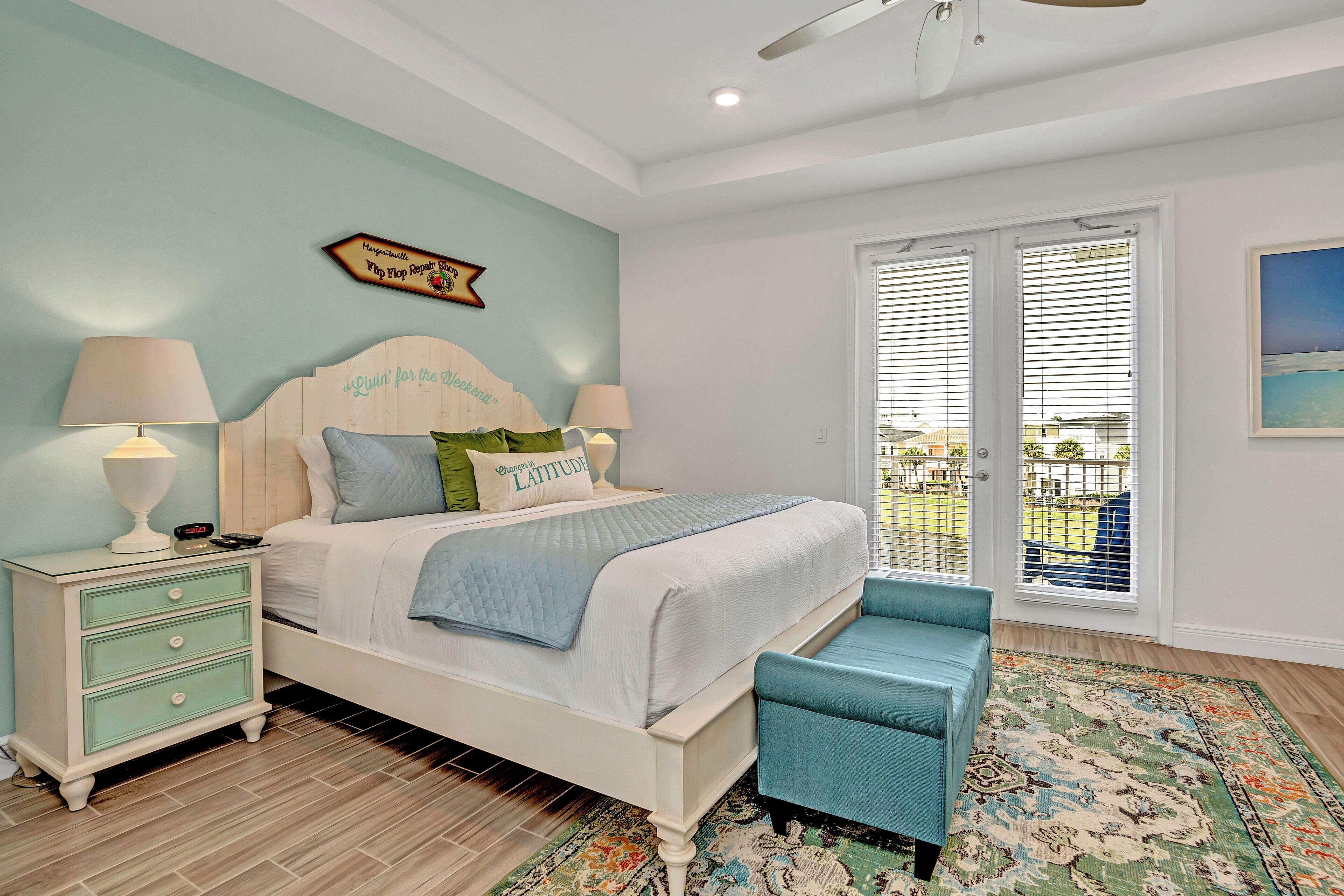 A bedroom with a bed, bedside tables, a bench, a patterned rug, and a balcony with a view.