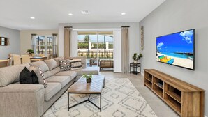 A modern living room with a large flat-screen TV, a sofa, a coffee table, and a TV stand. - Private Villa W/pool, Bbq,+free Water Park Access! (Kissimmee)