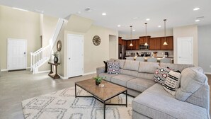 A spacious living room with a large sectional sofa, a coffee table, and a staircase leading to another level. - Private Villa W/pool, Bbq,+free Water Park Access! (Kissimmee)