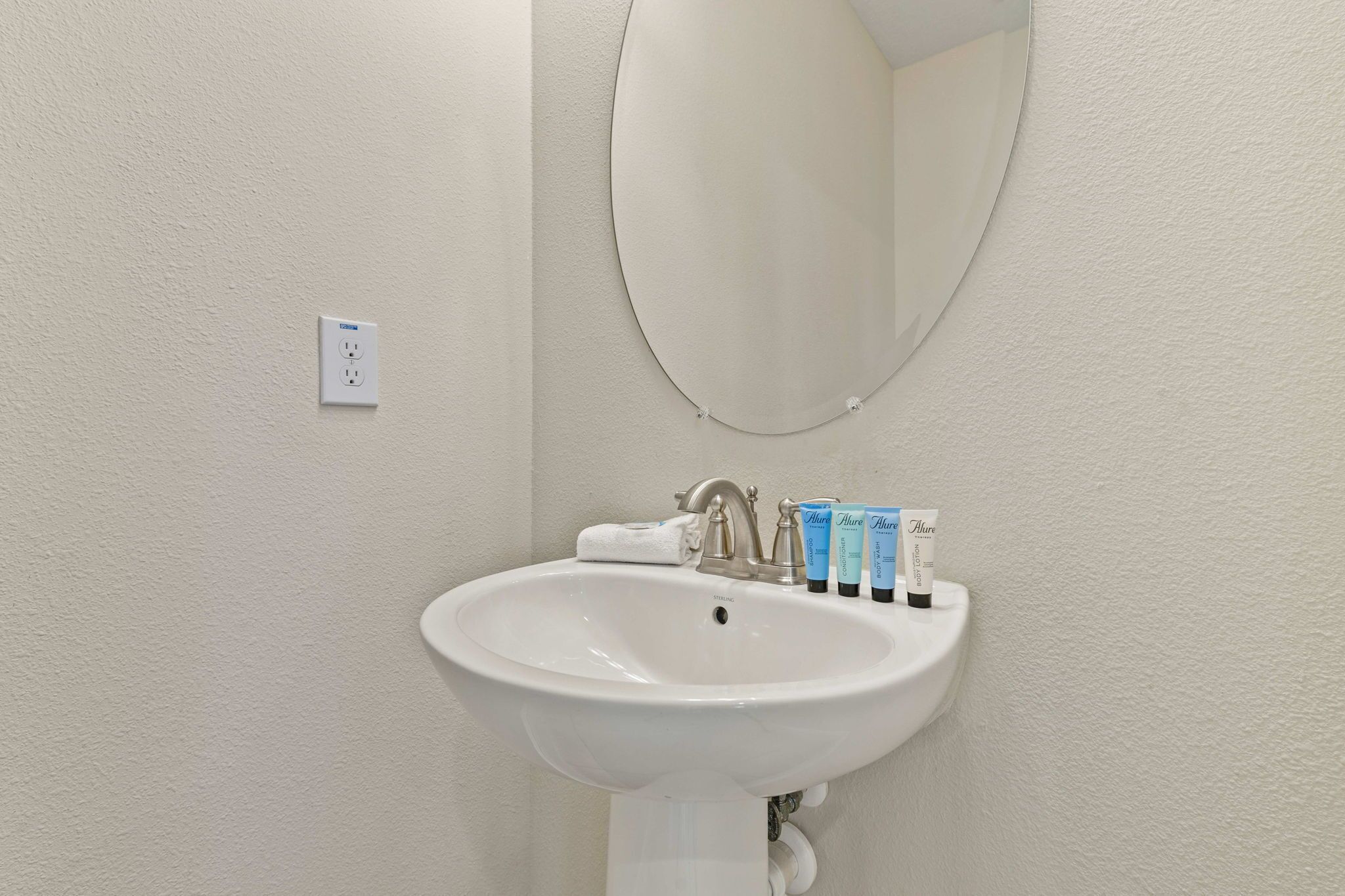 Un lavabo blanc dans une salle de bain, avec un miroir au-dessus et une serviette accrochée au mur.