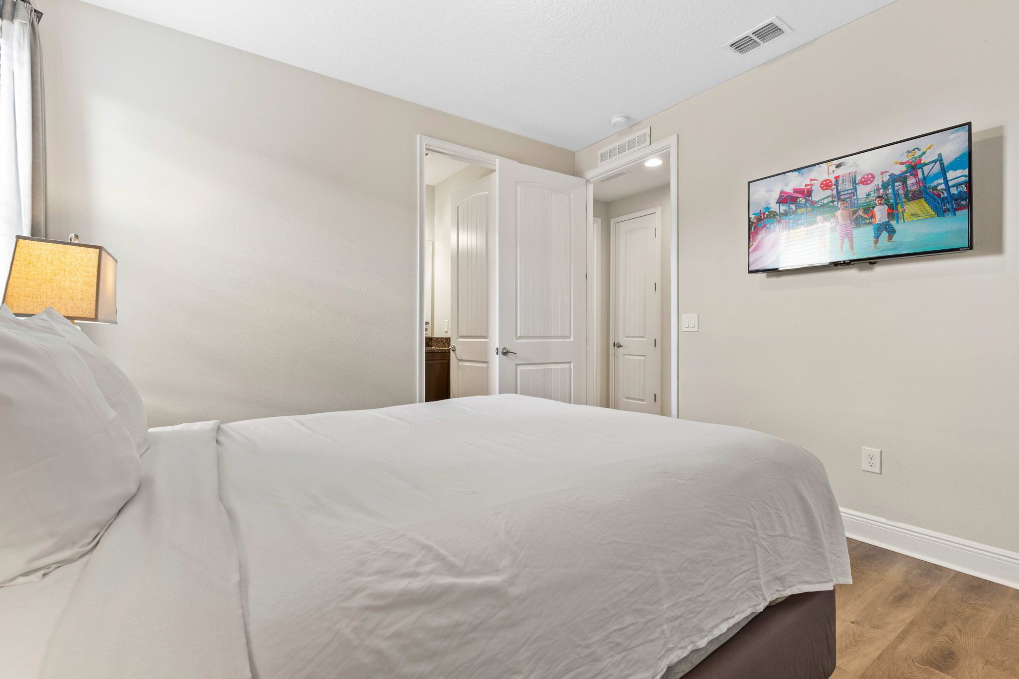 Een slaapkamer met een bed, een aan de muur bevestigde televisie en een deur naar een andere kamer.