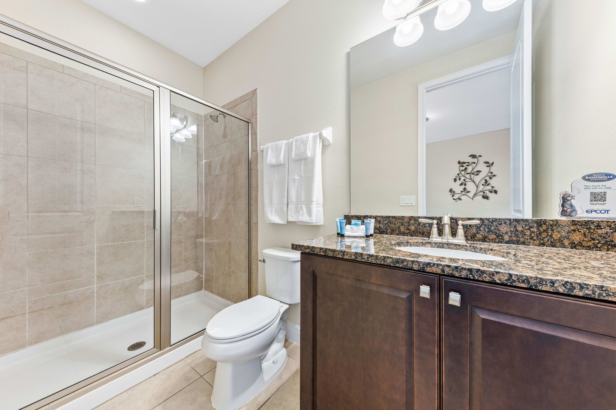 A modern bathroom with a glass shower enclosure, a white toilet, a vanity with a granite countertop, and a large mirror.