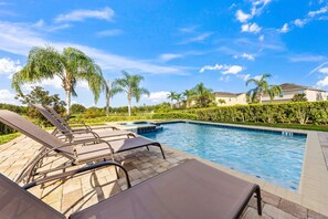A swimming pool with lounge chairs, palm trees, and a clear sky. - 7703 Banyon Way (Kissimmee)