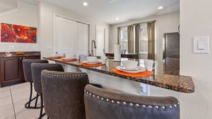 A modern kitchen with granite countertops, bar stools, and a large island. - 7703 Banyon Way (Kissimmee)